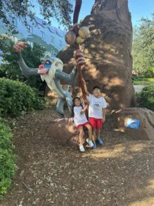 A boy and a girl in front of a life size statue of Rafiki from The Lion King.